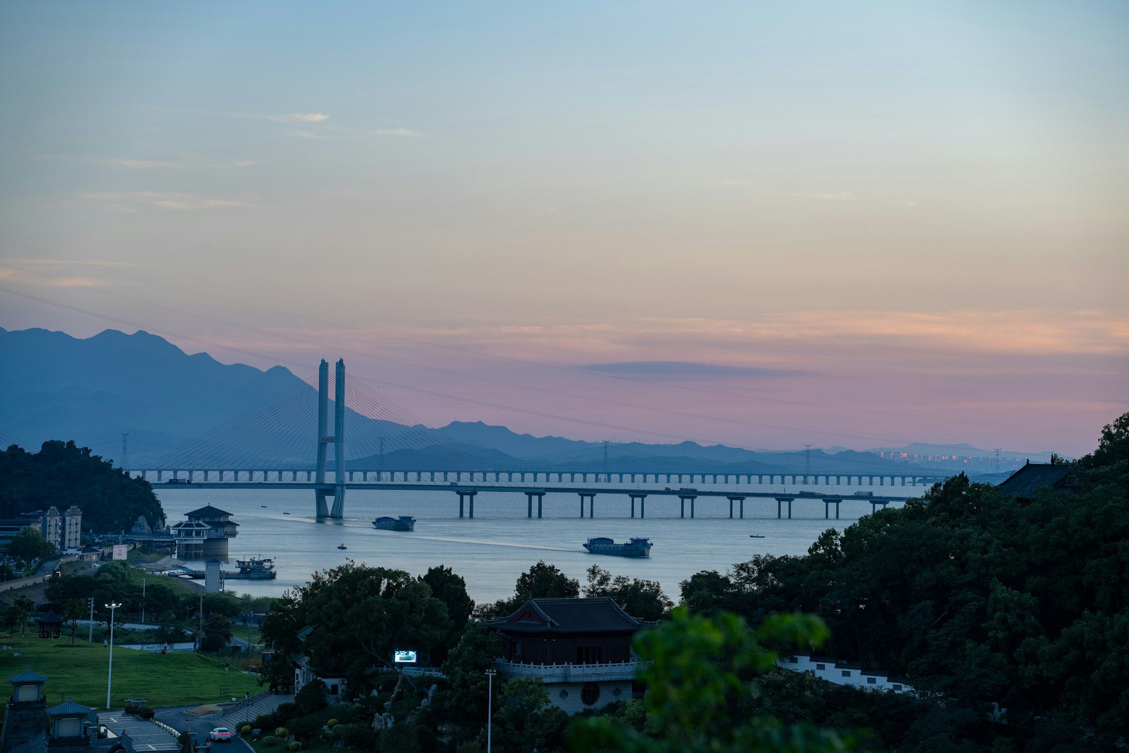 A long cable-stayed bridge across a river at dusk