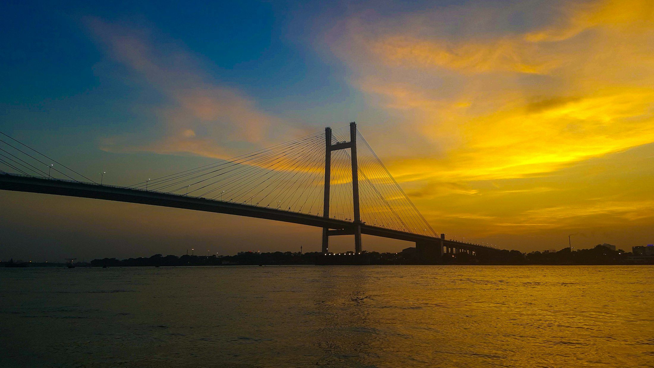 A cable-stayed bridge spanning a wide river at golden hour