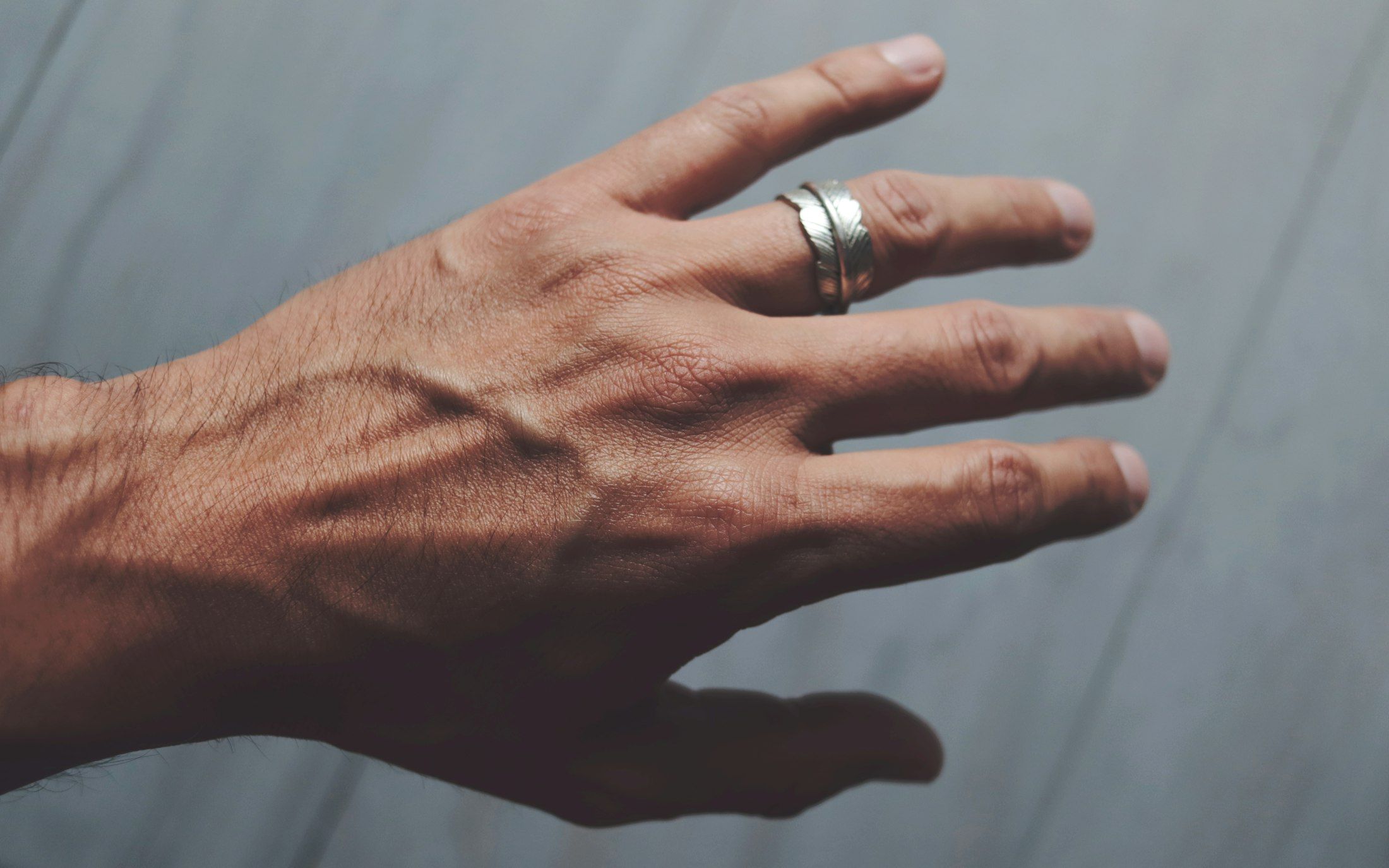 A man's hand wearing a plain sterling silver band