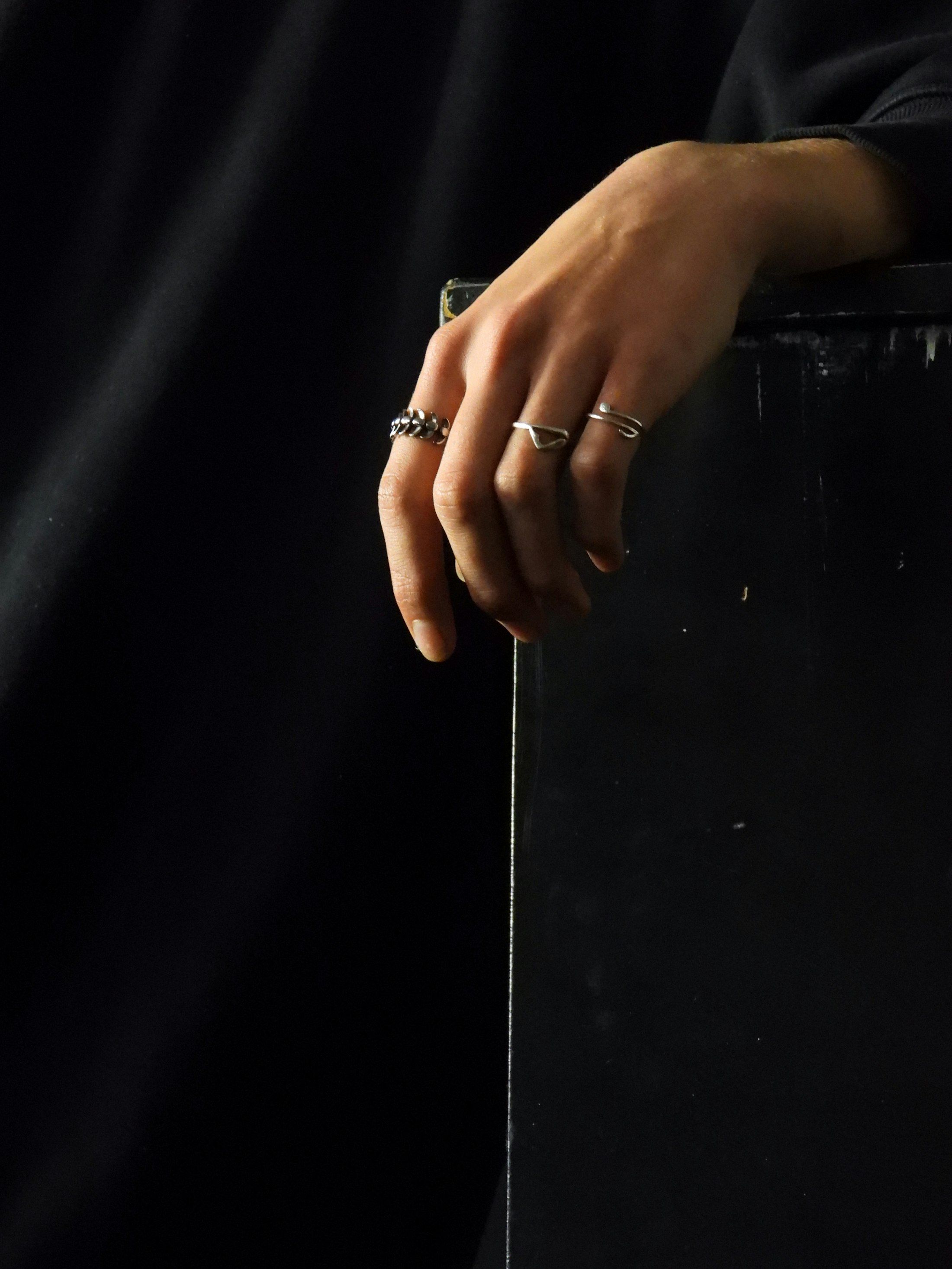 A hand wearing three minimalist silver rings against a black background