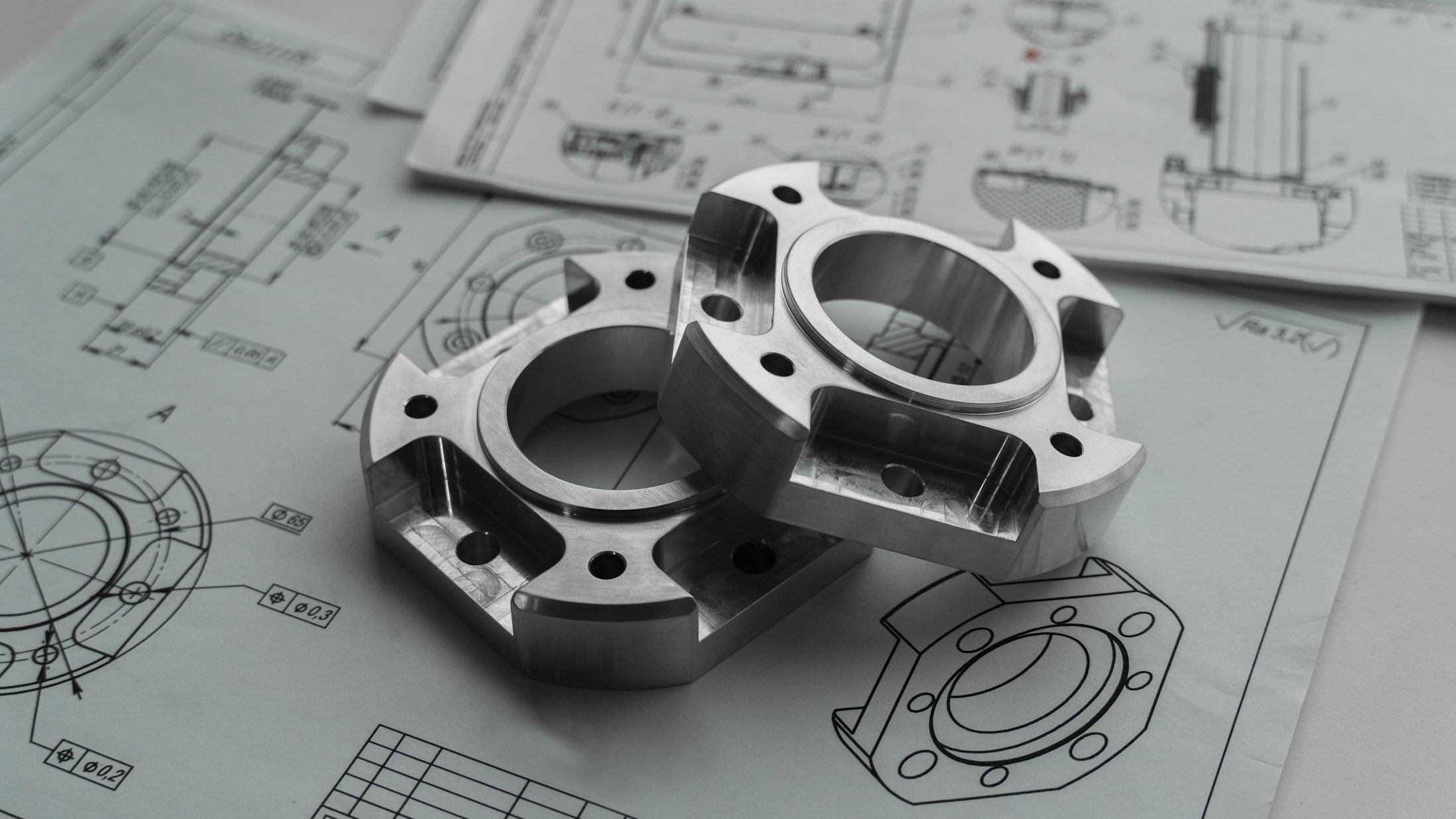 Two precision-machined metal parts lying on engineering drawings