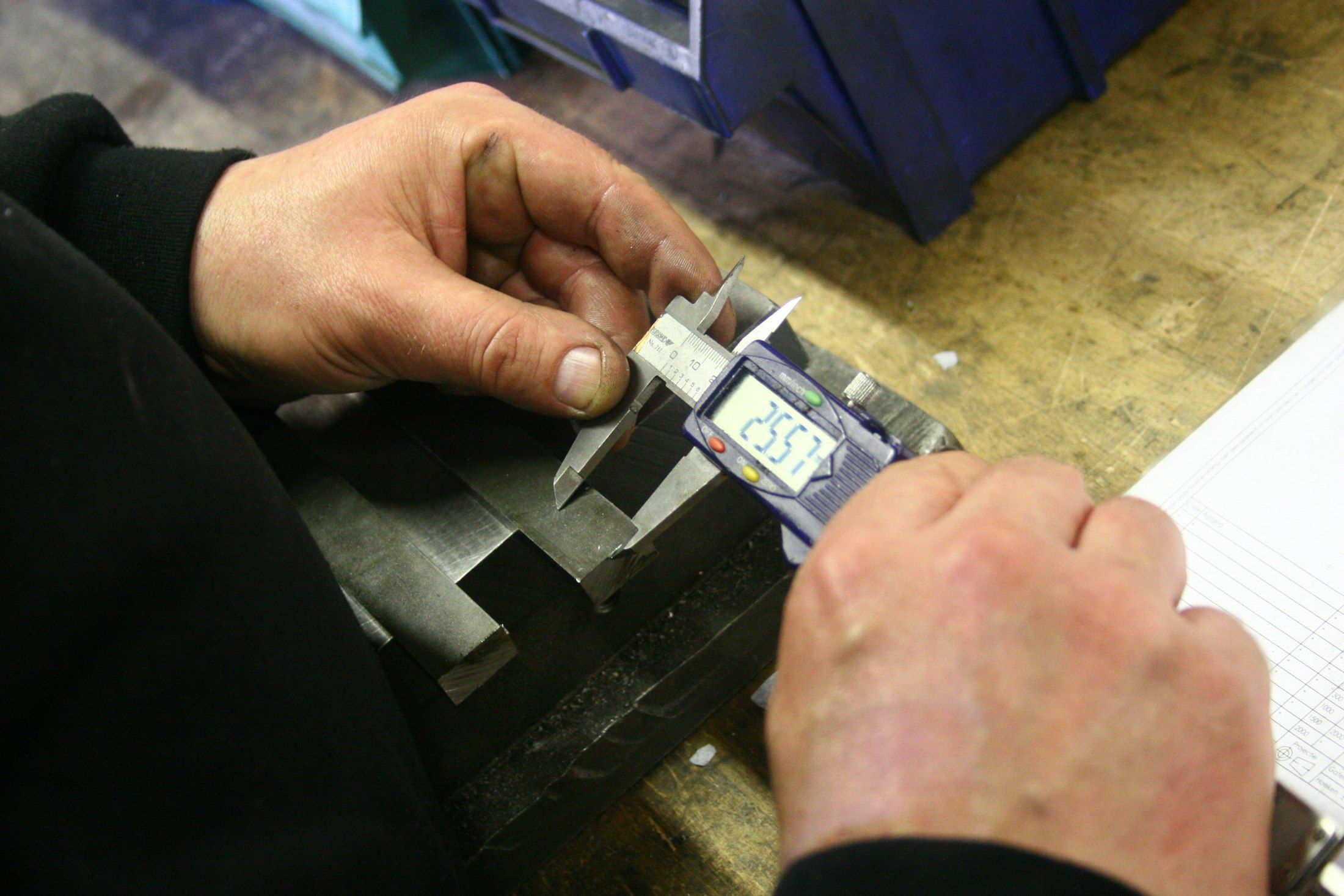 Hands measuring a machined metal part with a digital caliper