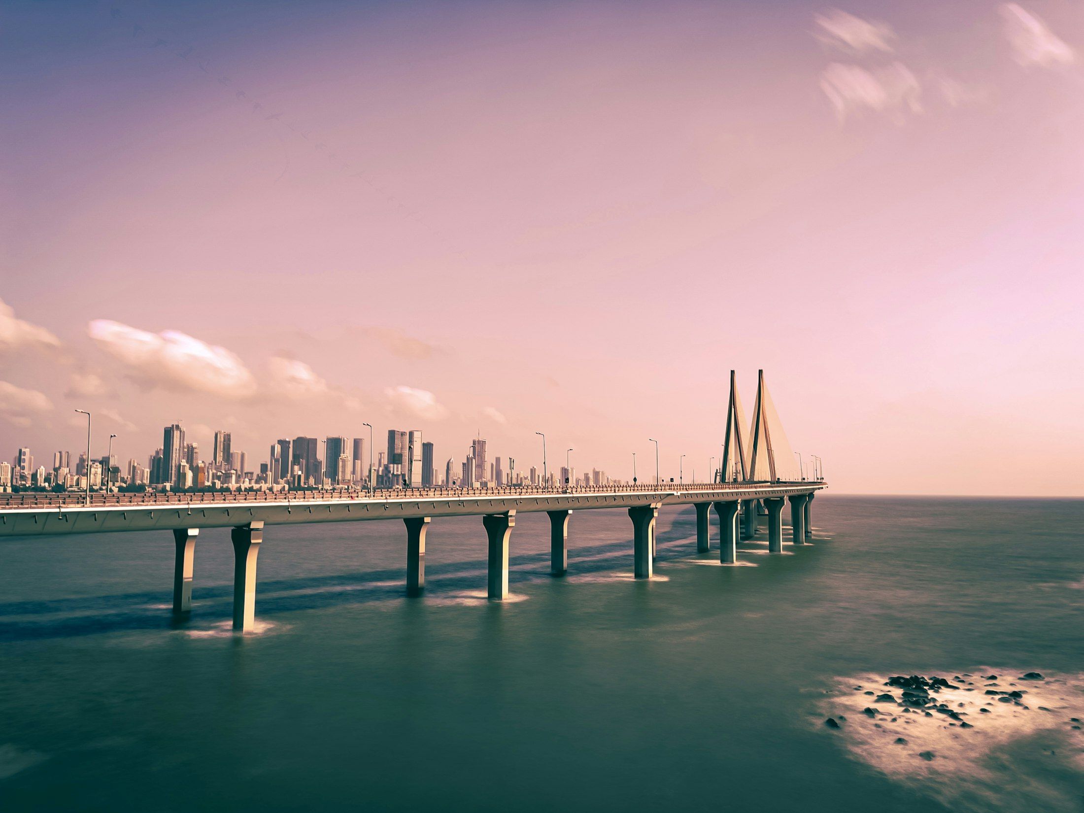 A long bridge across the water towards a city skyline at dawn