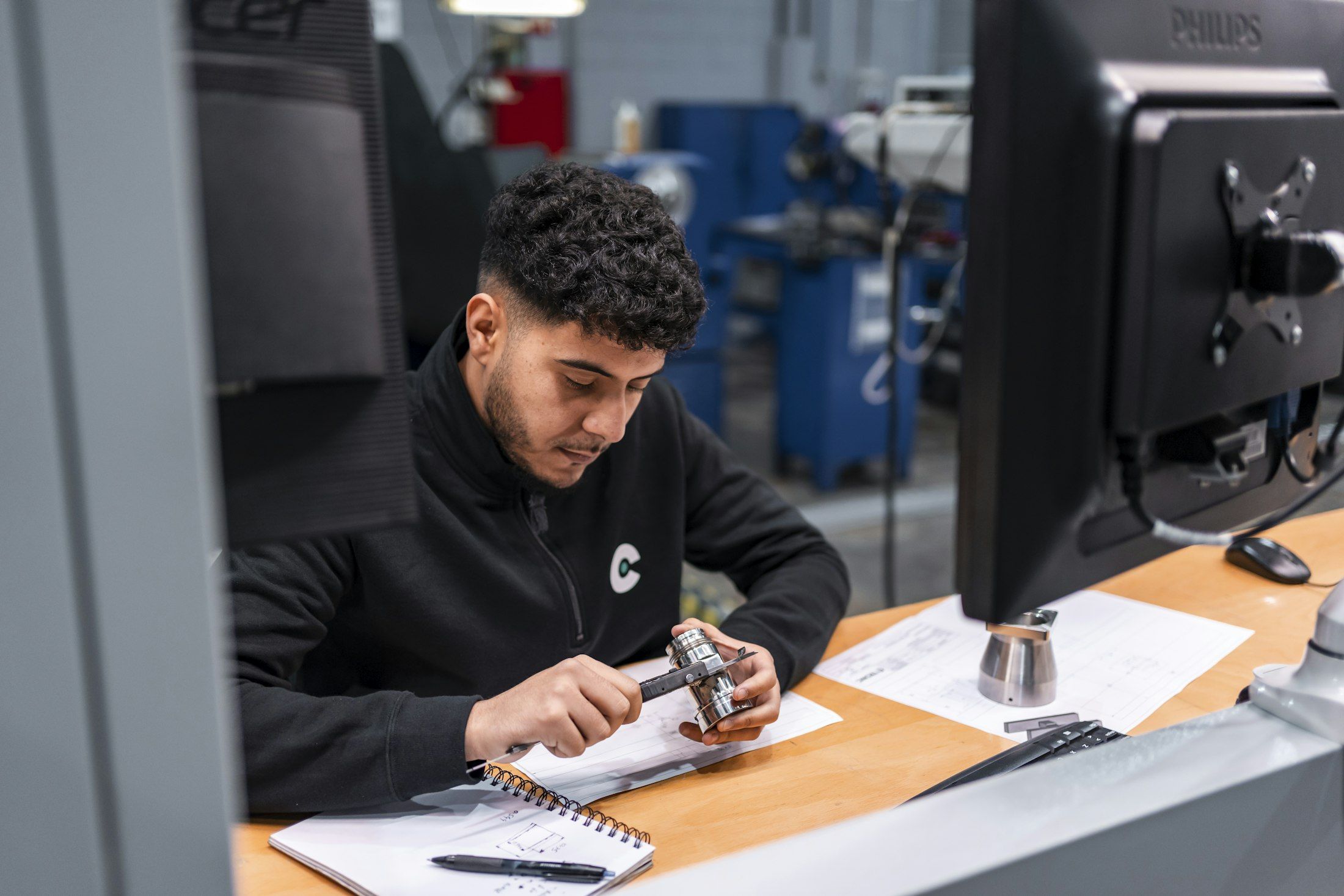 A technician carefully measuring a metal component at a workstation