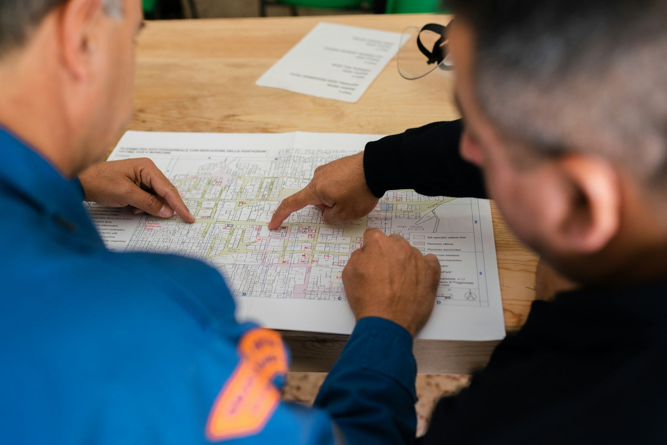Two engineers in work clothes reviewing printed plans at a table